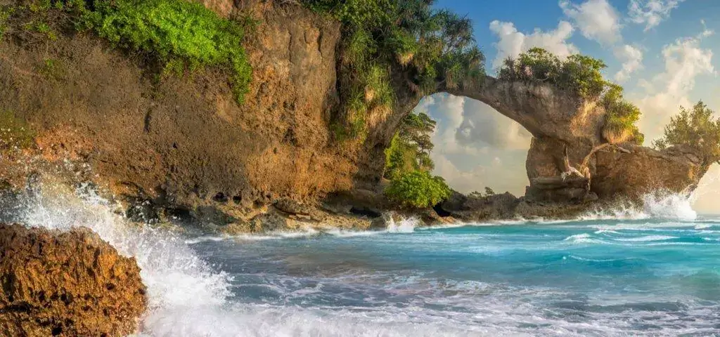 Natural rock arch over ocean with waves crashing, a must-see spot recommended by travel company in kolkata.