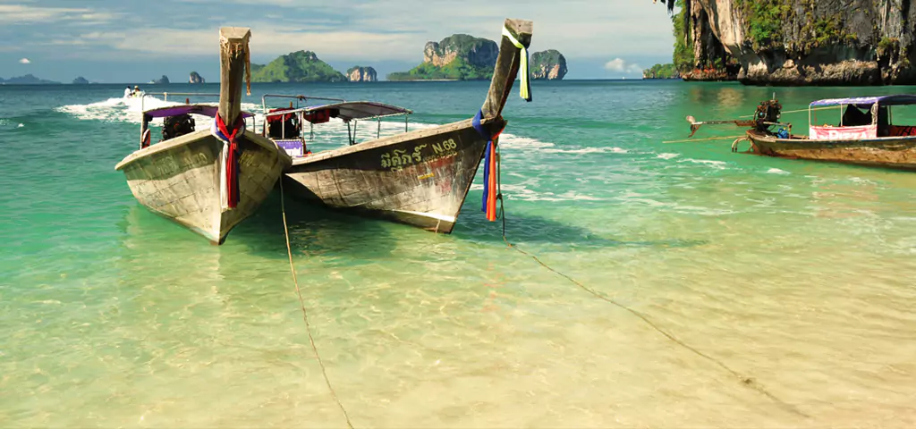 Traditional longtail boats on clear beach with cliffs, a featured scene in brochures from travel company in kolkata.